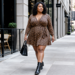 Emma Arletta Makes Monochrome Plus Size Style Look So Chic A stylish woman walks down a city sidewalk wearing a leopard print wrap dress, black ankle boots, and carrying a black handbag, showcasing confident urban street style.