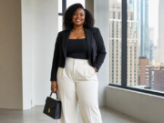 Plus Size Pear Shaped Body: Flattering Outfit Ideas and Styling Tips That Balance Your Silhouette A confident professional woman poses in a modern office wearing a black blazer, fitted top, wide-leg white trousers, pointed heels, and carrying a structured black handbag.