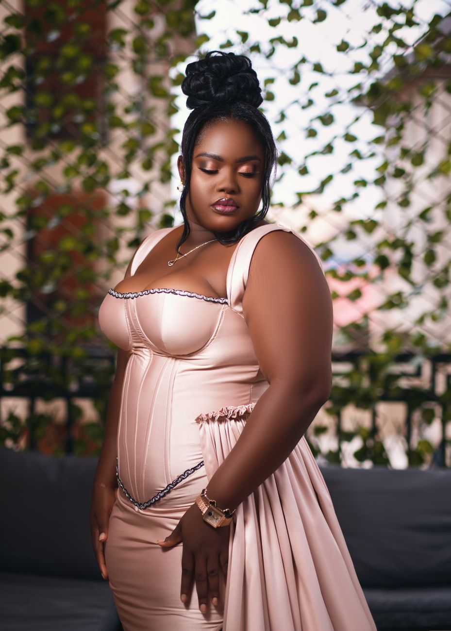 A beautiful plus-size African woman posing elegantly in a fashionable dress outdoors in Ghana.