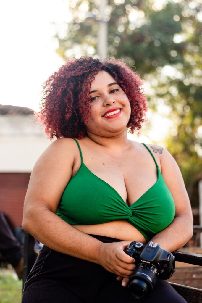 Confident woman posing with a camera outdoors, enjoying a sunny day.