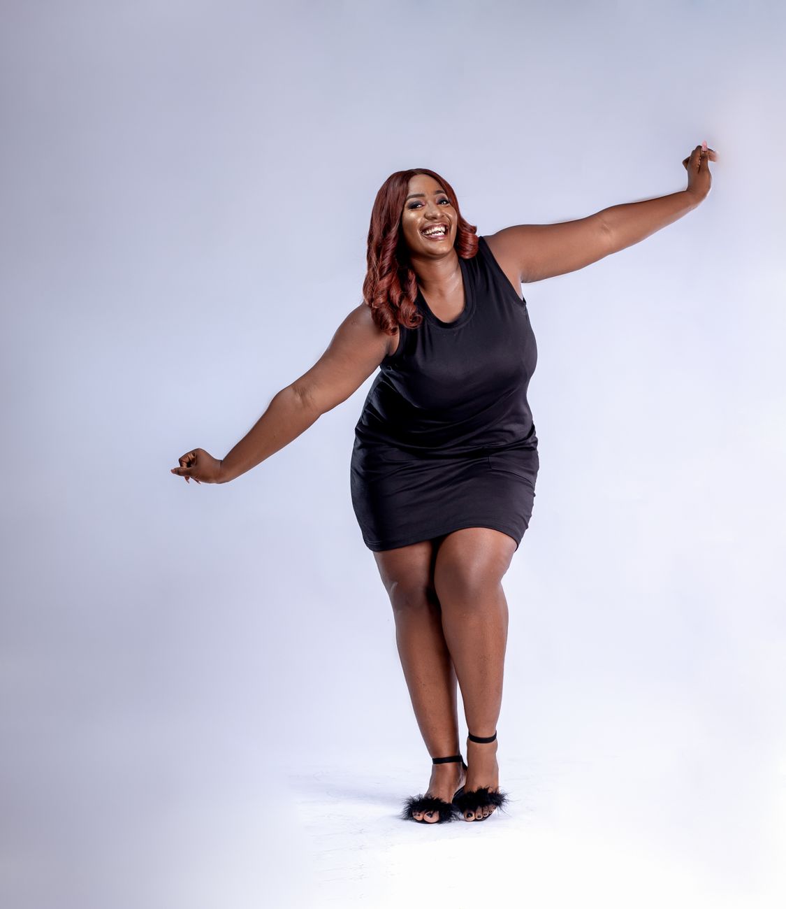 A joyful woman poses energetically in a black dress against a white studio background.